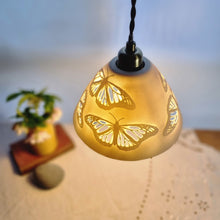 Load image into Gallery viewer, Porcelain Lampshade etched with Monarch butterflies. A vase with flowers, a book and a pebble in the background.