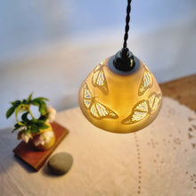 Load image into Gallery viewer, Porcelain Lampshade etched with Monarch butterflies. viewed from above. A vase with flowers, a book and a pebble in the background.