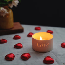 Load image into Gallery viewer, Creamy white porcelain tealight holder with the word Love etched into it. A glowing candle and chocolate hearts.
