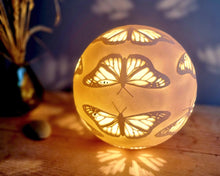 Load image into Gallery viewer, Glowing spherical light with butterfly designs on a wooden surface