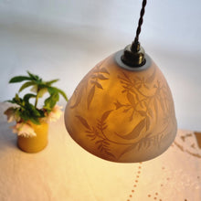 Load image into Gallery viewer, Handcrafted porcelain lampshade glowing gently, etched with swirling floral Jasmine design. Yellow vase with flowers in the background.