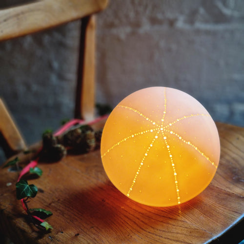 Spherical Porcelain Lamp Glowing warmly with sparkly starburst pattern made with dents and piercings.