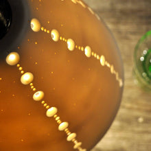 Load image into Gallery viewer, Detail of orange glowing bell shaped lampshade with lines of brighter dots running top to bottom. Vintage green stem glass on the right.