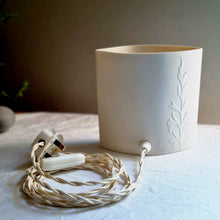 Load image into Gallery viewer, Elliptical porcelain lamp etched with Agapanthus. This image show the back of the piece, creamy white unlit porcelain with the braided switched cable.
