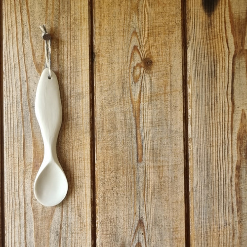 Sculpted porcelain spoon hanging on a wooden door.