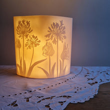 Load image into Gallery viewer, Porcelain lamp with coastal plant silhouettes designs etched onto it. It is glowing gently
