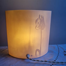 Load image into Gallery viewer, Porcelain lamp with coastal plant silhouettes designs etched onto it. It is glowing gently and shown from the back so you can see the cable going into it.
