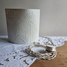 Load image into Gallery viewer, Porcelain lamp with coastal plant silhouettes designs etched onto it. Pure creamy white porcelain when unlit. Showing 2 metre braided switched cable and UK plug.
