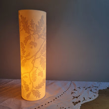 Load image into Gallery viewer, Porcelain cylinder Lamp etched with an Oak tree design in silhouette, glowing warmly.
