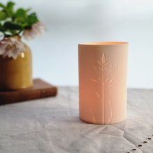 Load image into Gallery viewer, Porcelain Tealight holder with single grass flower etched into it. Glowing gently.
