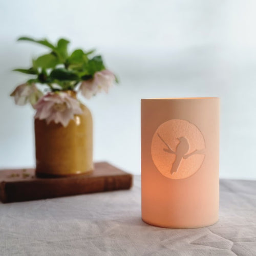 Glowing beaker with magpie silhouetted in a bright circle. Vase and pebble on left.