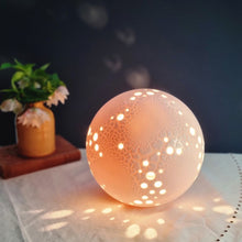 Load image into Gallery viewer, Pierced Porcelain lamp with textured glaze, lit, glowing warmly and projecting light spots
