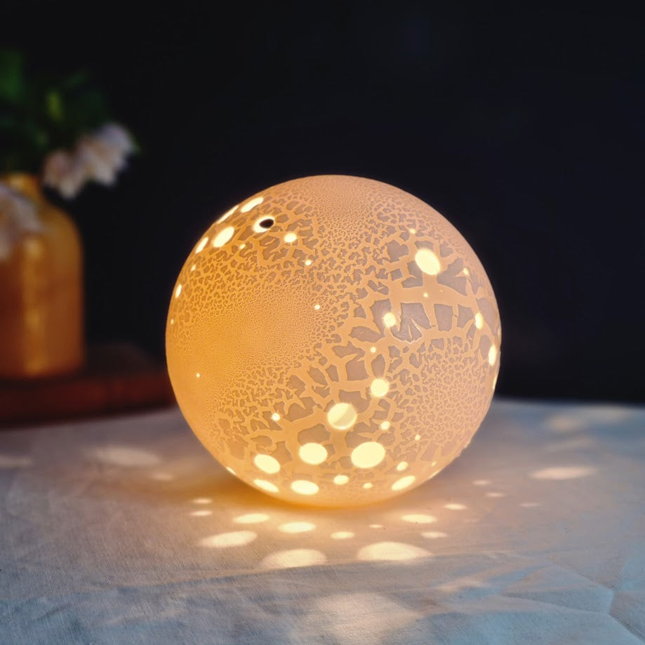 Porcelain Lamp with textured surface and round holes casting lightspots around it.