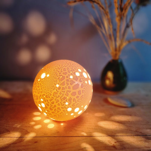 Glowing spherical lamp with random piercings and textured surface, casting spots of light all around it.