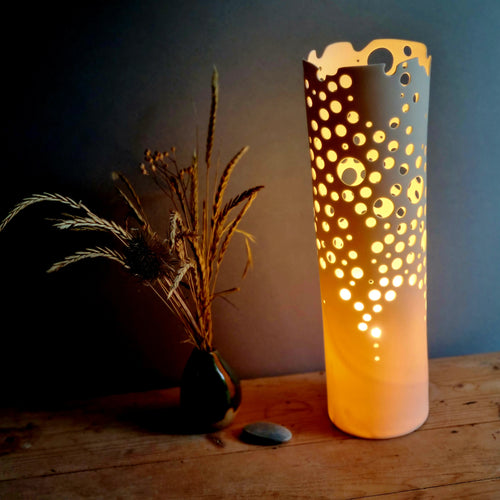 Cylindrical lamp glowing orange with many holes pierced into it.