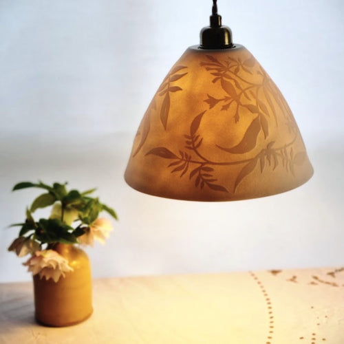 Porcelain Lampshade glowing gently, etched with swirling Jasmine design. Yellow vase with flowers in the background.
