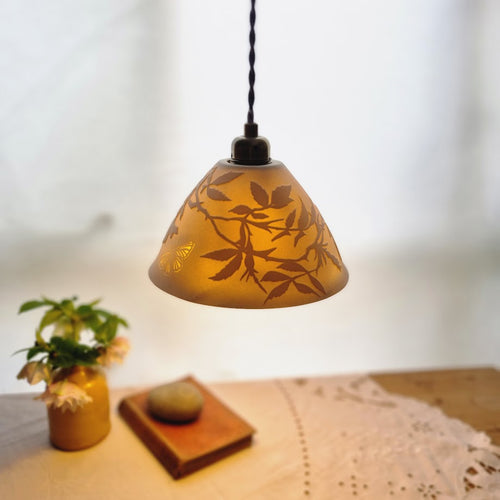 Porcelain Lampshade etched with wild roses and a butterfly. A vase with flowers, a book and a pebble in the background.