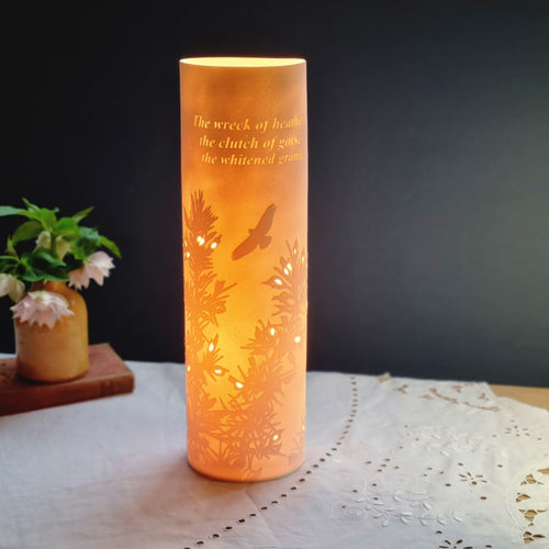 Porcelain cylinder Lamp etched with Gorse design in silhouette and words from the James Goodman poem Clay country. glowing warmly.