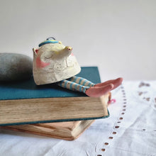 Load image into Gallery viewer, Stoneware creature character with stripey legs reclining on some books..
