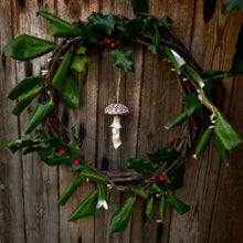 Load image into Gallery viewer, Wreath with green leaves and red berries hanging on a wooden door, ceramic fly agaric mushroom in the centre.
