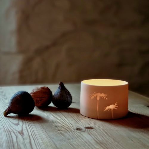 Translucent Porcelain pot with tealight glowing in it, two figs and a walnut on the left.