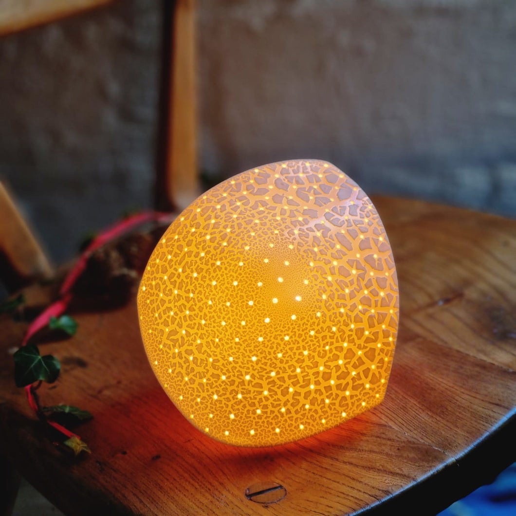 Glowing textured asymetrical diamond shaped lamp with regularly spaced pinpricks of light. 