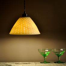 Load image into Gallery viewer, Orange sparkly bell shaped lampshade with small bright dots running from top to bottom. Two green glasses on the right.
